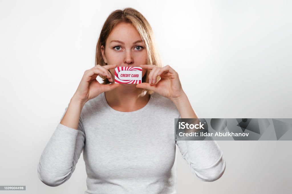 Shopping and Finance. Beautiful young woman holds in hands a credit card at the level of the lips. White background and copy space Shopping and Finance. Beautiful young woman holds in hands a credit card at the level of the lips. White background and copy space. Credit Card Stock Photo