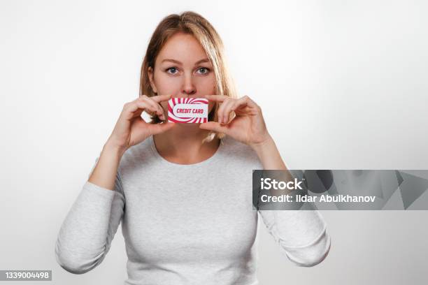 Shopping And Finance Beautiful Young Woman Holds In Hands A Credit Card At The Level Of The Lips White Background And Copy Space Stock Photo - Download Image Now