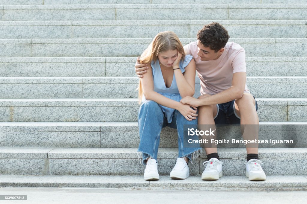 Troubles in teenager relationships Teenager couple sitting on the stairs. Hispanic boyfriend trying to cheer up and hugging sad girlfriend. Relationship troubles, anxiety and depression in adolescence concept with copy space. Couple - Relationship Stock Photo