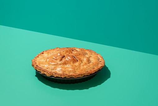 Freshly baked apple cake in minimalist on a green table with harsh shadow. Homemade apple pie with a delicious golden crust.