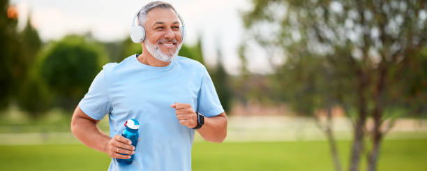 счастливый зрелый мужчина в наушниках с бутылкой воды в руке jo - aging process morning outdoors horizontal стоковые фото и изображения