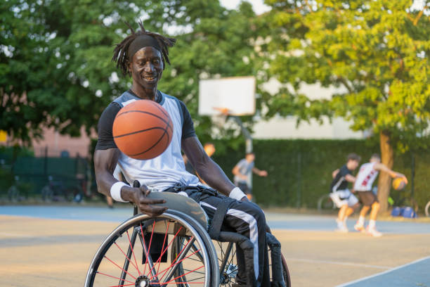 uomo africano con disabilità causata dalla poliomielite che gioca a basket, atleta campione con disabilità su una sedia a rotelle, concetto di determinazione e forza mentale - basket su sedia a rotelle foto e immagini stock