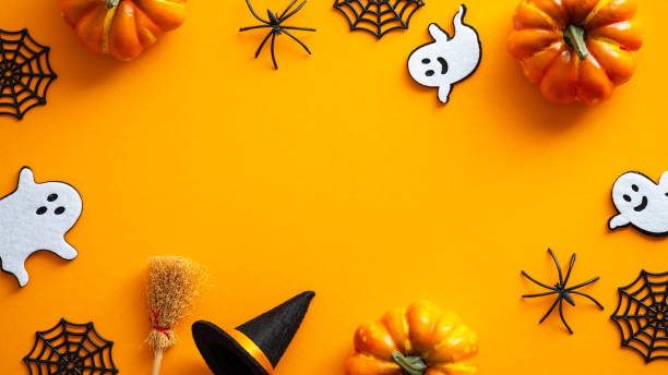 istock Happy Halloween card design mockup. Flat lay, top view ghosts, spider web, pumpkins, witch hat and broom on orange background. 1339010405
