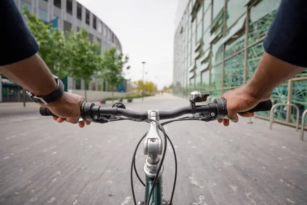A point of view shot from an unrecognisable mature black man wearing formal businesswear on a summers day in a city. He is riding bicycle as he sustainably commutes to work.