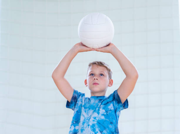 体育のレッスンでバレーボールをしている学校の子供。水平教育ポスター、グリーティングカード、ヘッダー、ウェブサイト。パンデミックコンセプト中に学校に安全に戻る - volleying sport indoors action ストックフォトと画像
