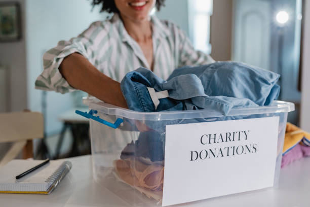 Packing clothes in donation box for charity organization Photo of a woman at home, she is preparing clothes for donation clothing donation stock pictures, royalty-free photos & images