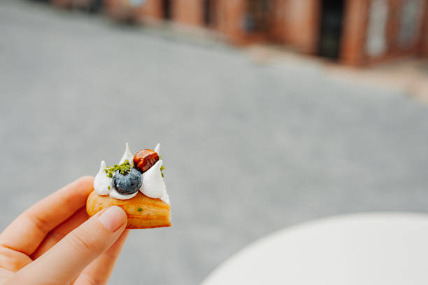 the bit off part in hand, delicious beautiful eclair with white cream, fresh blueberries and caramel on the table of an outdoor cafe. selective focus