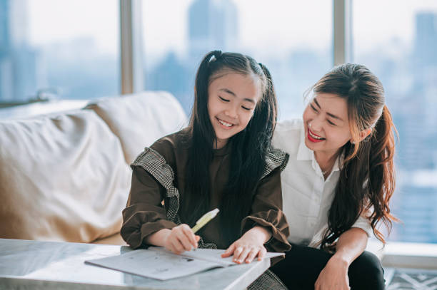 asian chinese young family mother daughter enjoying bonding time doing homework  at home during weekend in living room apartment asian chinese young family mother daughter enjoying bonding time doing homework  at home during weekend in living room apartment parents and kids studying stock pictures, royalty-free photos & images