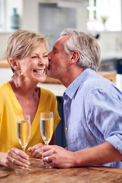 kissing retired couple celebrating with glass of champagne at home on date night together - date night imagens e fotografias de stock