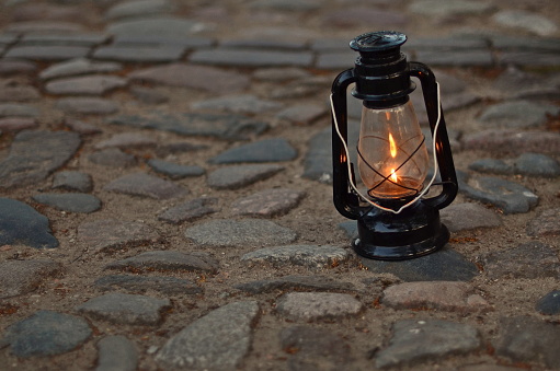 A lit kerosene lamp stands on the pavement late at night
