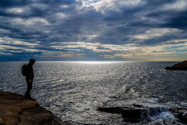 istock Man with backpack standing on a rock watching the sea. 1339016138