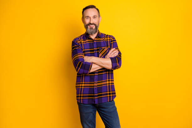 retrato fotográfico de un anciano feliz y sonriente hombre de negocios con camisa con las manos dobladas aisladas sobre un fondo de color amarillo vivo - one mature man only fotografías e imágenes de stock