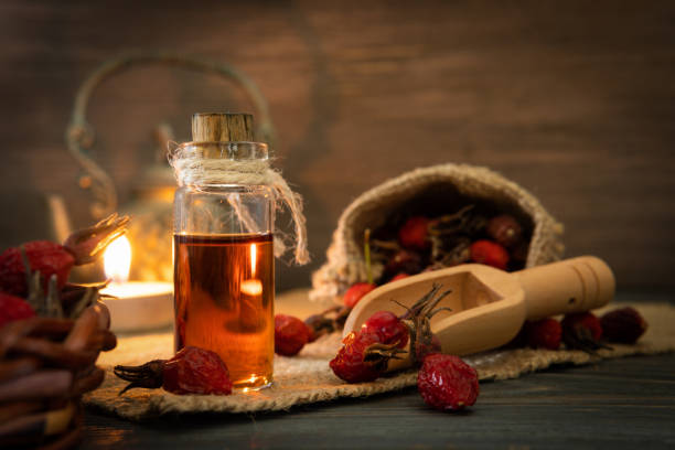 Rosehip oil on wooden background with red fruits Rosehip oil on wooden boards on a dark background. The bottle is tied with a cord with dogrose essential oil. Bag of berries. wild rose hip stock pictures, royalty-free photos & images