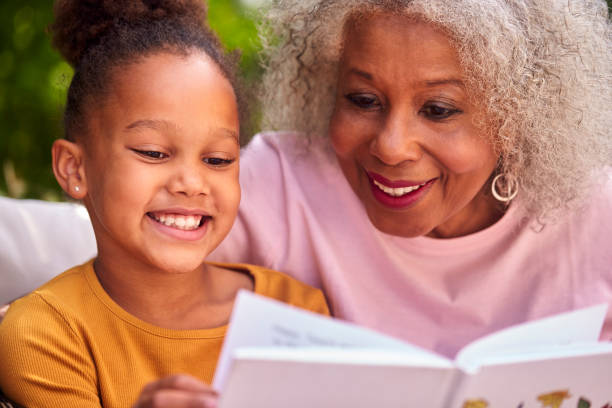 grandmother sitting outdoors with granddaughter at home reading book together - family reading african descent book imagens e fotografias de stock