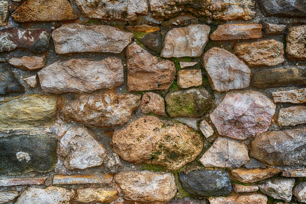 cobblestone wall, old and weathered, gray and brown covered with green moss - color image solid brown bumpy imagens e fotografias de stock
