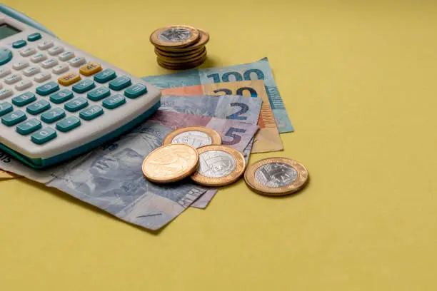 Photo of Brazilian money, coins and calculator on yellow background. Financial control