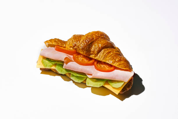 istock Croissant sandwich with mortadella, cheese, arugula and scrambled eggs. Hard light. White background 1339020384