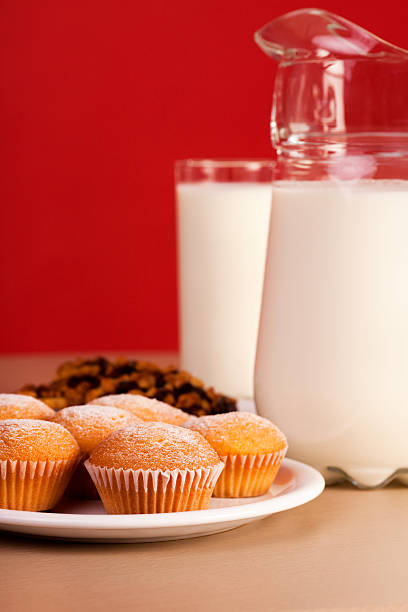 Close-up of a plate of muffins, with a pitcher and a glass of milk in the background, over red background