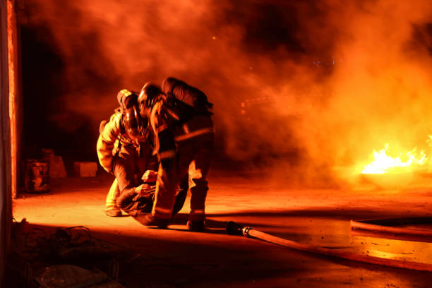 Team of firemen helping one injured firefighter. Fire in the background.