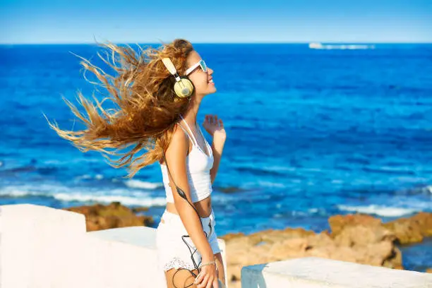 Blond kid teen girl hearing headphones music on smartphone in a beach