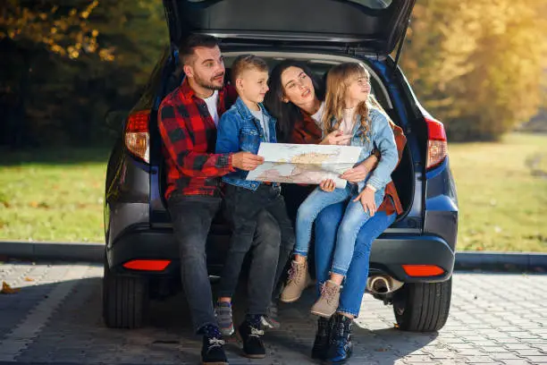 Photo of Close up of joyful pleasant family which gethering on their vacation with teen children and using road map to choose the right path on the car