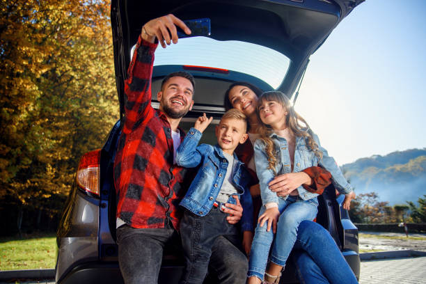 glückliche stilvolle eltern mit ihren süßen, lieben kindern machen lustige selfies auf dem smartphone, während sie im kofferraum sitzen. glückliches modernes familienkonzept. - auto kofferraum stock-fotos und bilder