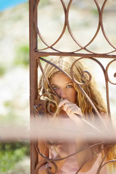 Blond girl in Mediterranean rusted gate with sea in background