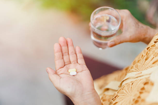 An old woman's hand holds a pill and a glass of drinking water for eat. Health care concept. An old woman's hand holds a pill and a glass of drinking water for eat. Health care concept. morning after pill stock pictures, royalty-free photos & images