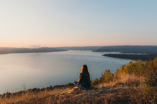 Young woman with long hair in pyjama waking up with the fjord-like lake viewpoint, enjoying the sunny fall sunset outdoors