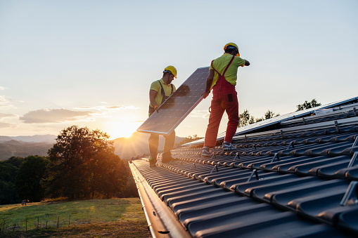 Trabajadores instalando paneles solares en casa de madera en la naturaleza al atardecer. photo