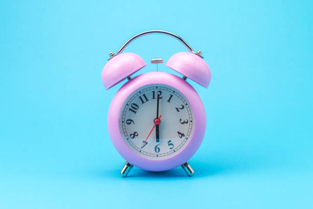 istock Pink alarm clock on blue background 1339036990