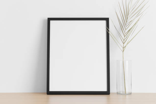 istock Black frame mockup with a palm leaf on the wooden table. 1339037338