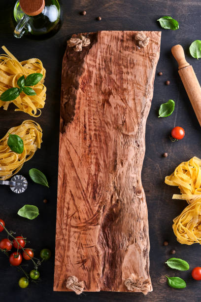 Tagliatelle. Homemade pasta, basil leaves, flour, pepper, olive oil, cherry tomato and rolling pin and pasta knife on dark old wooden background. Food concept. Mock up. Horizontal with copy space.