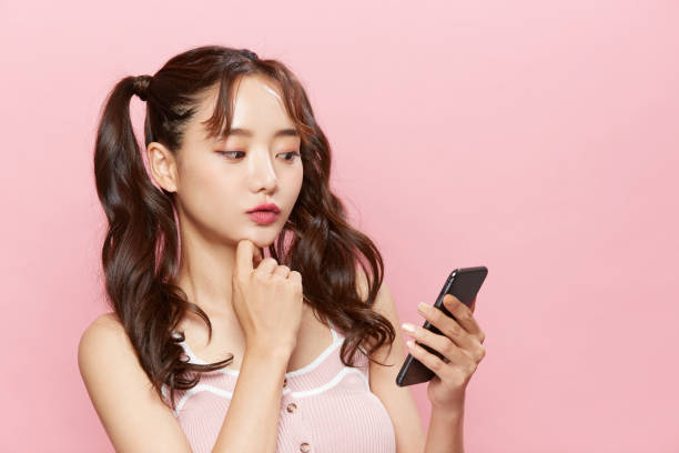 Portrait of a young woman operating a smartphone on a pink background Studio Pigtails stock pictures, royalty-free photos & images