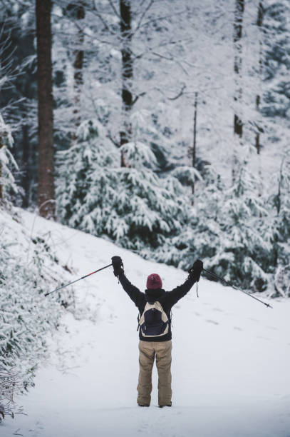 Woman with hiking poles standing in winter scenery, arms spread wide