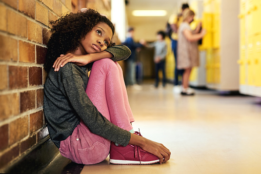 Foto de cuerpo entero de una niña sentada en el pasillo de la escuela y sintiéndose deprimida photo