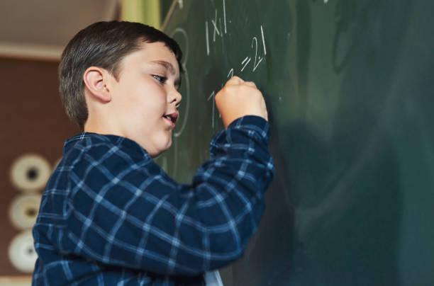 shot of a young boy standing alone and writing on the blackboard during a lesson in his classroom at school - education blackboard africa youth culture imagens e fotografias de stock