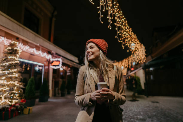 Photo of a young woman drinking hot drink and  walking through the town during the Christmas holidays