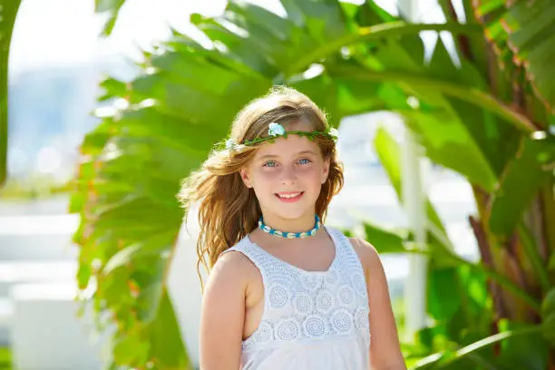 Blond kid girl at banana tree leaves in bright day light in Mediterranean