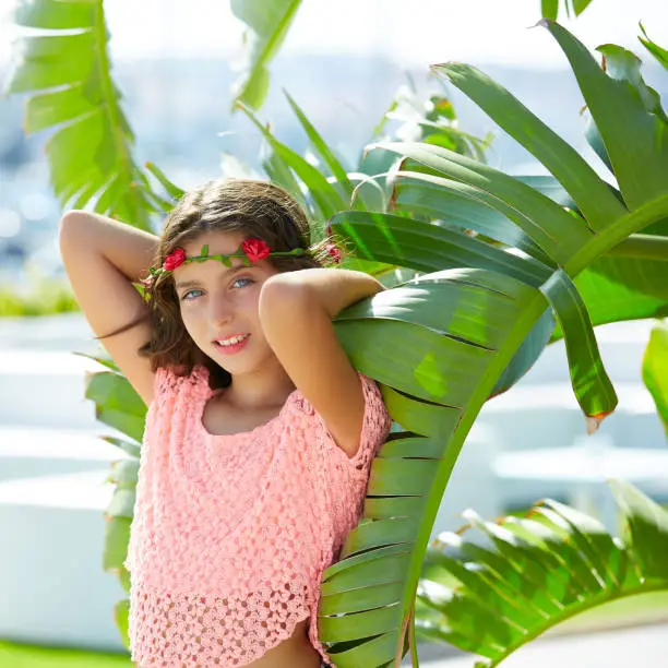 Brunette kid girl at banana tree leaves in bright day light in Mediterranean