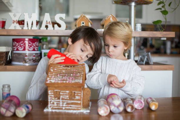 Children, boys, decorating home made ginger bread house at home with candies