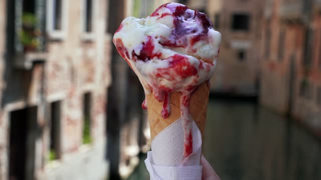 A hand holding an ice cream gelato on a waffle cone against gondolas