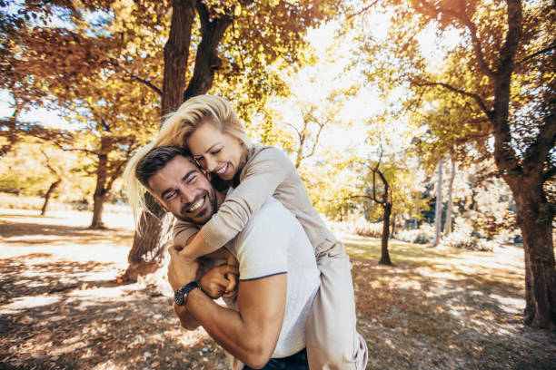 namorado carregando sua namorada em piggyback no parque de outono. - couple in love - fotografias e filmes do acervo