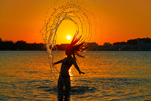Girl flipping hair flip at sunset beach in orange sky