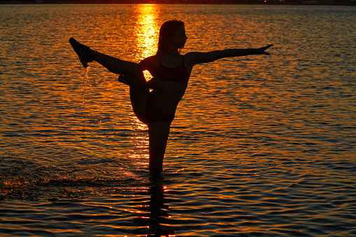 Girl gymnastics pose at sunset beach in orange sky