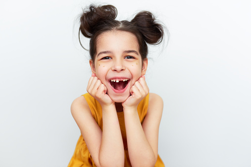 The overjoyed preschool little girl in yellow dress showing empty space with growing first permanent molar isolated on grey studio background. Happy kid missing baby tooth. A child has lost milk tooth
