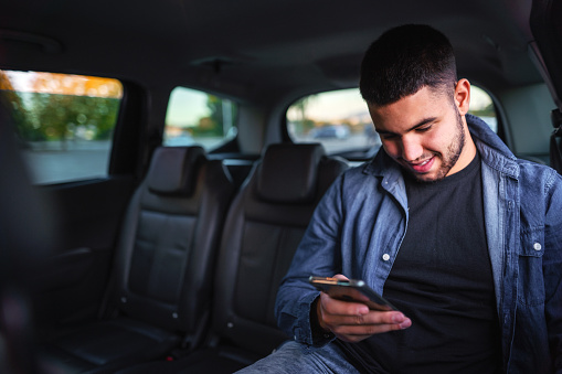 Young Adult Man Waiting For Uber and Text Messaging on back Seat of a Car