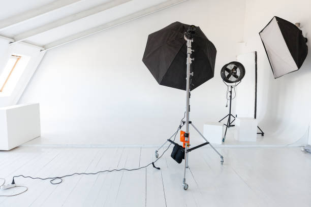 istock Empty photo studio with lighting equipment. Photographer workplace interior with professional tool set gear. Flash light white background scenes ready for studio shooting. Modern photographer studio 1339053299