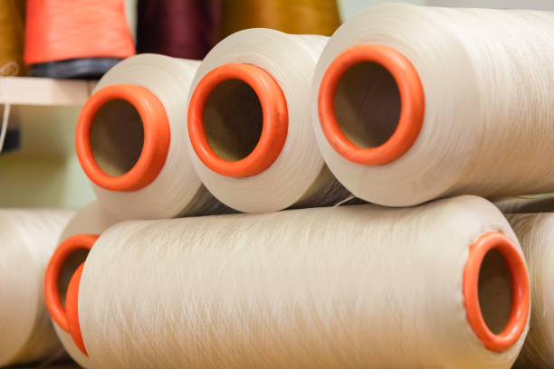 istock A row of large industrial bobbins with synthetic beige threads. 1339055409