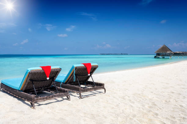 istock Two sun beds on a tropical beach with christmas hats 1339057754